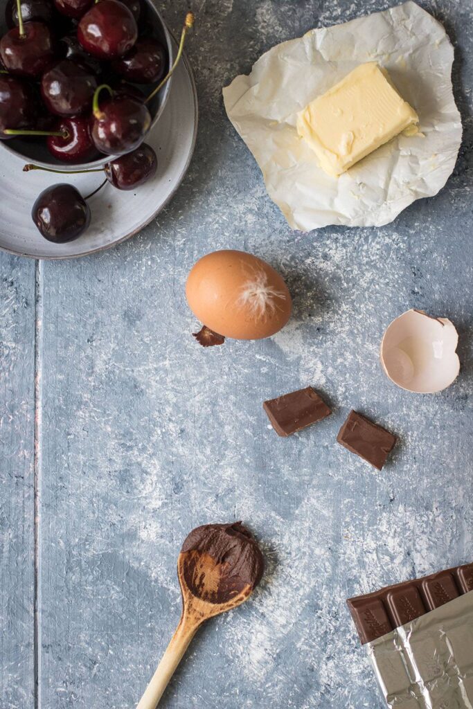 Kirschen, Eier, Butter und Schokolade für saftigen Schokokuchen auf Tisch