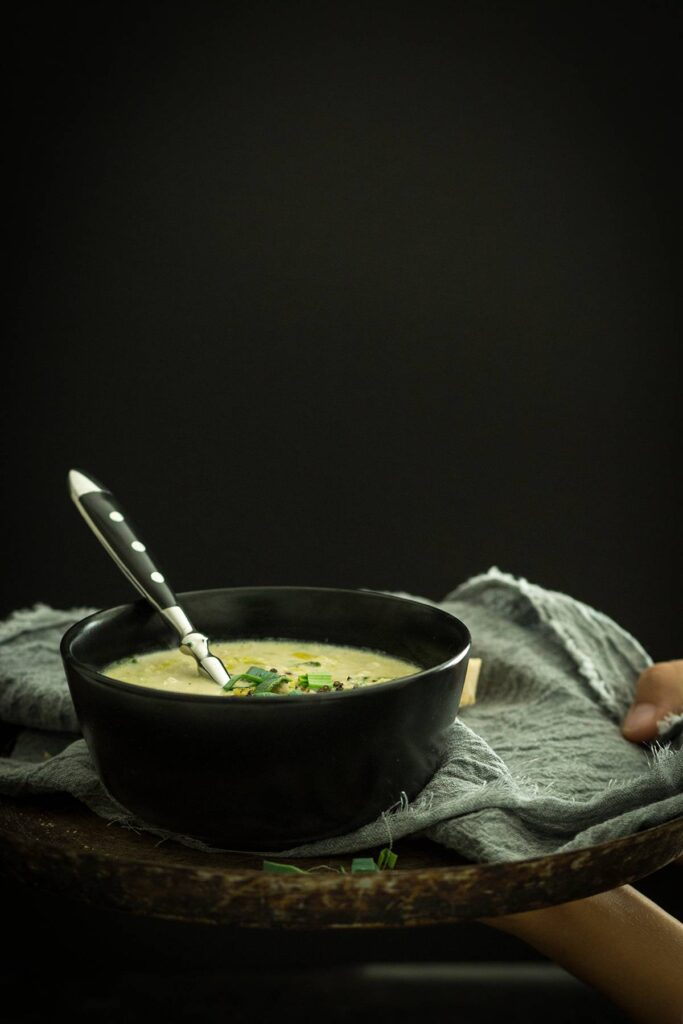 Käse-Lauch-Suppe mit Löffel in Schüssel auf Holzbrett serviert
